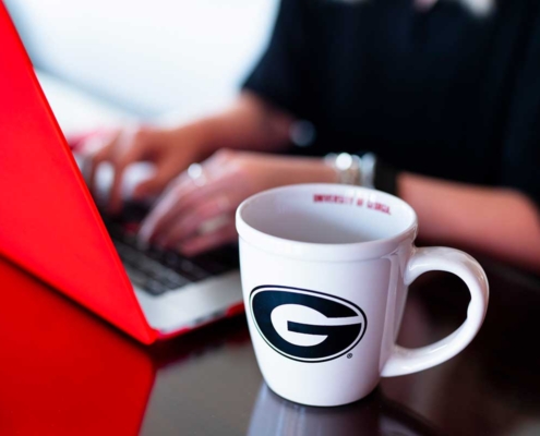 Hands on keyboard with a UGA mug