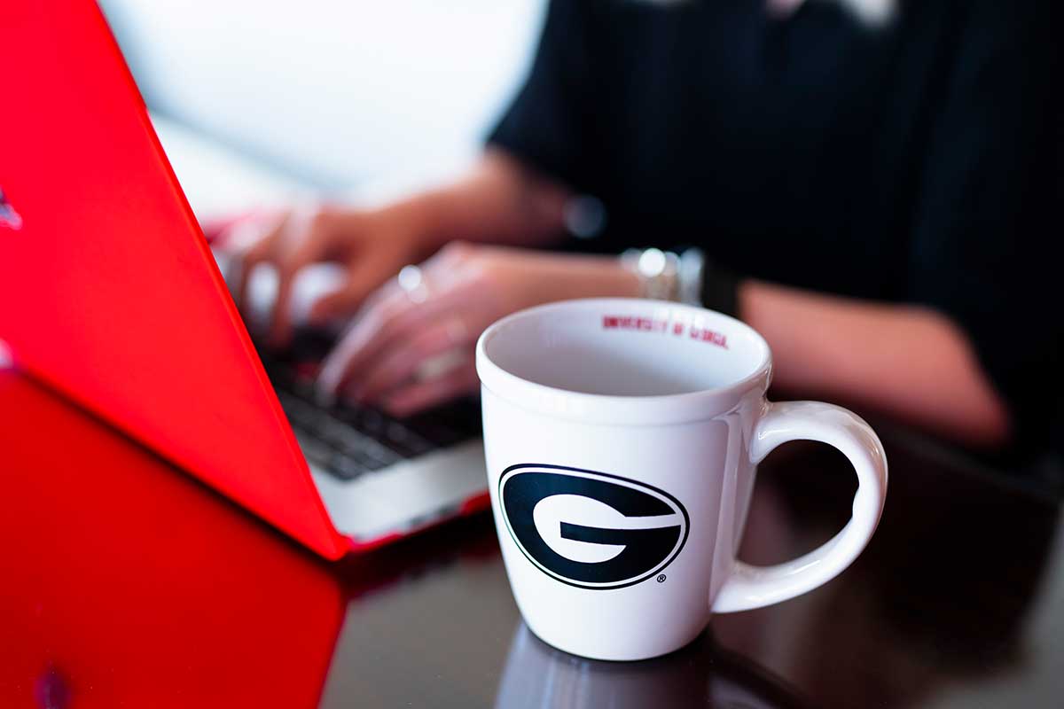 Hands on keyboard with a UGA mug