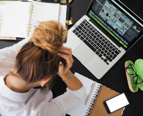 Woman with hands on head looking down at her laptop and phone on the table