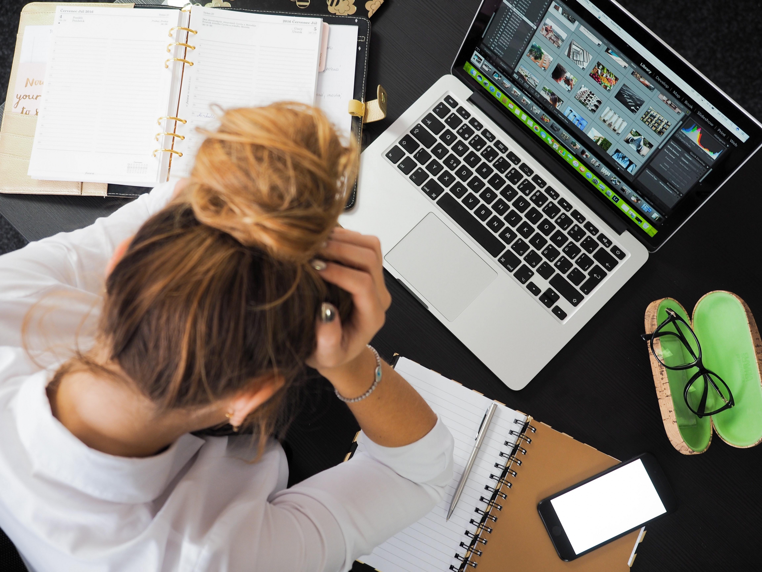 Woman with hands on head looking down at her laptop and phone on the table